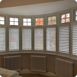 Full-height white shutters installed across a curved bay window